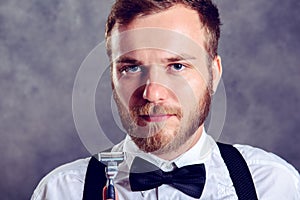 Bearded man in white shirt and bow tie showing shaver