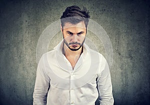 Bearded man in white shirt looking with anger and offense at camera on gray background