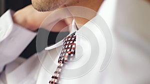 Bearded man in white shirt tying a tie. Close up