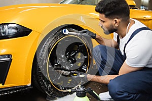 Bearded man worker washing car alloy wheel and tires on a car wash