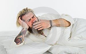 Bearded man yawning lying on soft white pillow. Handsome man in bathrobe yawning waking up in cozy bed at home in