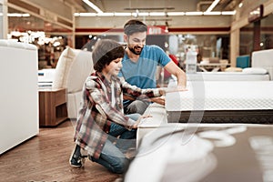 Bearded man with young son is testing mattress for softness. Testing softness of mattress.