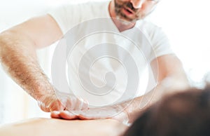 Bearded Masseur man doing massage manipulations on the Scapula area zone during young female body massaging