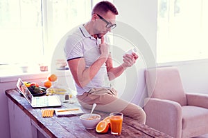 Bearded mature man wearing glasses hesitating about drinking food supplements