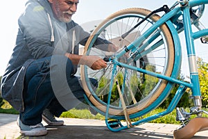 Bearded mature man wearing jeans and sport jacket repairing his blue bicycle