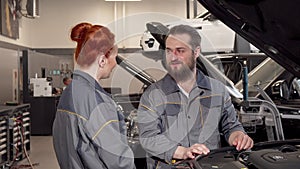 Bearded mechanic talking to his female coleague at the automobile workshop