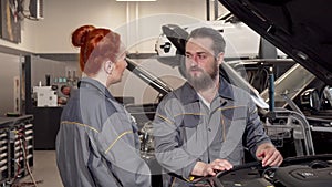 Bearded mechanic talking to his female coleague at the automobile workshop