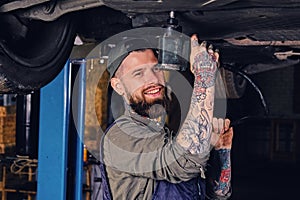 Bearded mechanic working with the car`s chassis in a workshop.