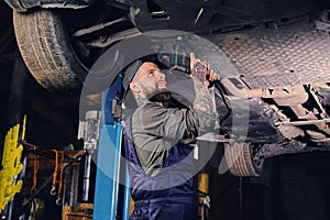 Bearded mechanic working with the car`s chassis in a workshop.