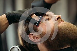 Bearded man with long beard getting stylish hair shaving , haircut , with razor by barber in barbershop