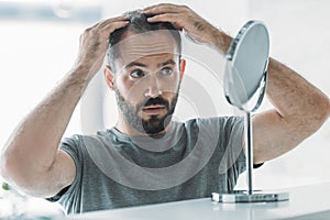 bearded mid adult man with alopecia looking at mirror hair