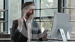 Bearded middle-aged business man in office sitting table using phone mobile audio app service to listening music singing