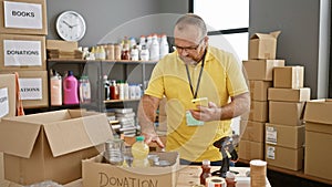Bearded, middle-aged, handsome caucasian man is a dedicated volunteer at the charity center, engrossed in checking products using