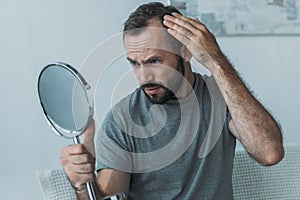 bearded middle aged man with alopecia looking at mirror hair loss