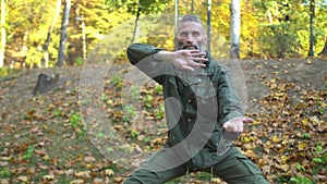 Bearded middle-aged man in khaki clothes doing chinese tai chi exercises on lawn in autumn city park