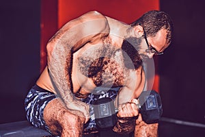 Bearded muscular man working out with dumbbells weights in a gym