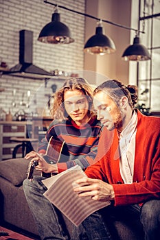 Bearded music tutor wearing red cardigan teaching his student