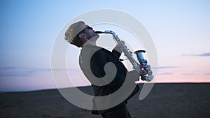 bearded musician in sunglasses and black jacket performs his part on beautiful shiny saxophone at sunset or sunrise with