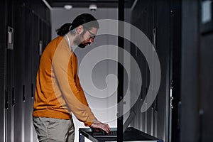 Bearded network engineer using laptop in server room