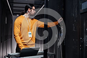 Bearded network engineer using laptop while working in server room