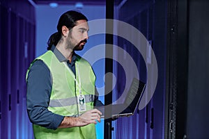 Bearded network technician working with servers in neon light