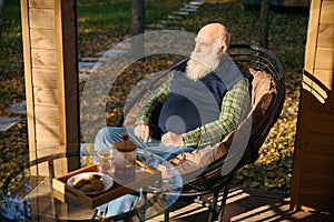 Bearded old man is having tea on the veranda