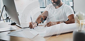 Bearded professional architect wearing eye glasses working at modern loft studio-office with desktop computer.Blurred