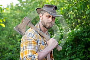 bearded rancher with axe wearing checkered shirt. rancher with axe outdoor.