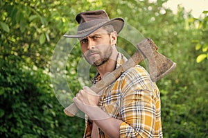 bearded rancher with axe wearing checkered shirt. rancher with axe outdoor.