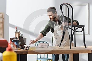 Bearded restorer in apron holding taking