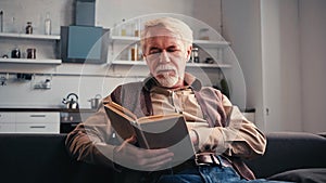 bearded retired man reading book at