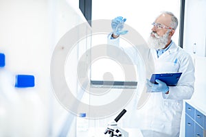 Bearded scientist holding flask with reagent and clipboard in chemical lab