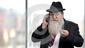 Bearded senior businessman negotiating on mobile phone.