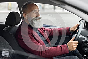 Bearded senior man driving luxury car, shot inside vehicle