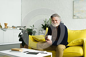 bearded senior man holding cup of coffee and smiling at camera