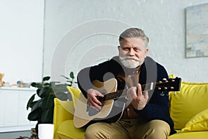 bearded senior man playing guitar and smiling at camera