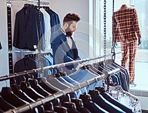 Bearded shop assistant dressed in blue elegant suit working in menswear store.