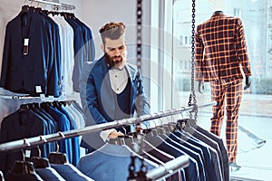 Bearded shop assistant dressed in blue elegant suit working in menswear store.