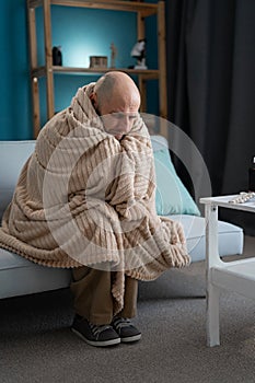 Bearded sick man with flue sitting on sofa covering in blanket. Illness, influenza, pain concept.