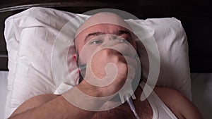 of a bearded sick man lies on the bed, opens his eyes and removes the ventilator from his face