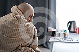 Bearded sick sad man wrapping blanket sits on couch suffers from flu disease. Unwell guy feeling bad fever virus illness