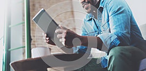 Bearded smiling African man using tablet for video conversation while relaxing on sofa in modern office. Concept of young