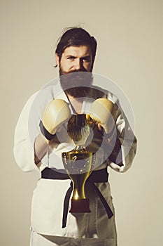 Bearded smiling karate man in kimono, boxing gloves, champion cup