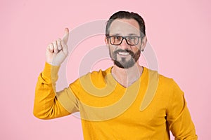 Bearded smiling man in glasses pointing up on pink background. Happy sales manager with finger up. Wise Man in glasses notices