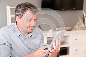 Bearded smiling man using tablet for video conversation while relaxing on sofa in modern house in Concept of business people