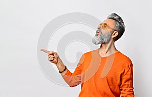 Bearded and stylish. Handsome smiling bearded man in orange sweater and sunglasses, bracelet showing direction with finger.