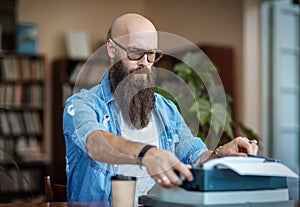 Bearded stylish writer typing on typewriter