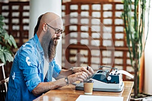 Bearded stylish writer typing on typewriter