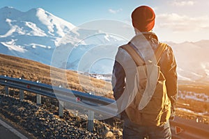 Bearded tourist hipster man in sunglasses with a backpack stand back on a roadside bump and watching the sunset against