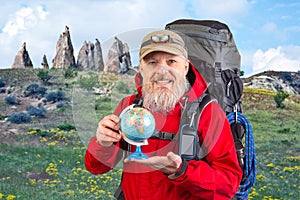 bearded tourist in a red jacket holds a model of the world globe in his hands. tourism and travel around the world